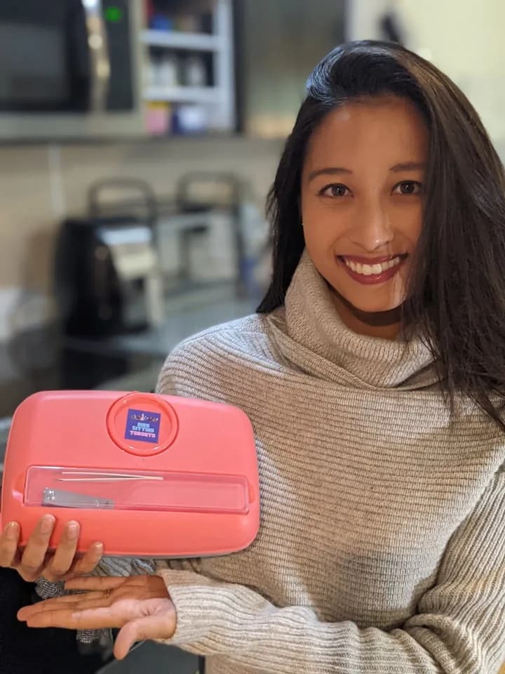 Samantha smiling in a grey turtleneck, holding up her pink Bird Sitting Toronto first aid kit