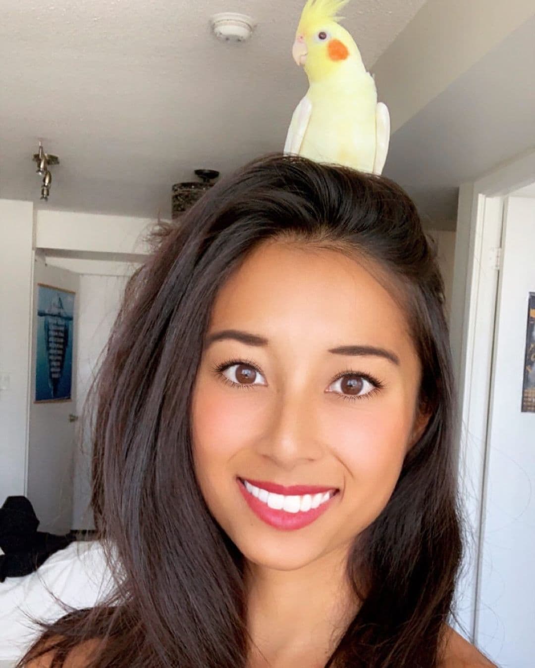 Samantha smiling, with a cockatiel perched on top of her head