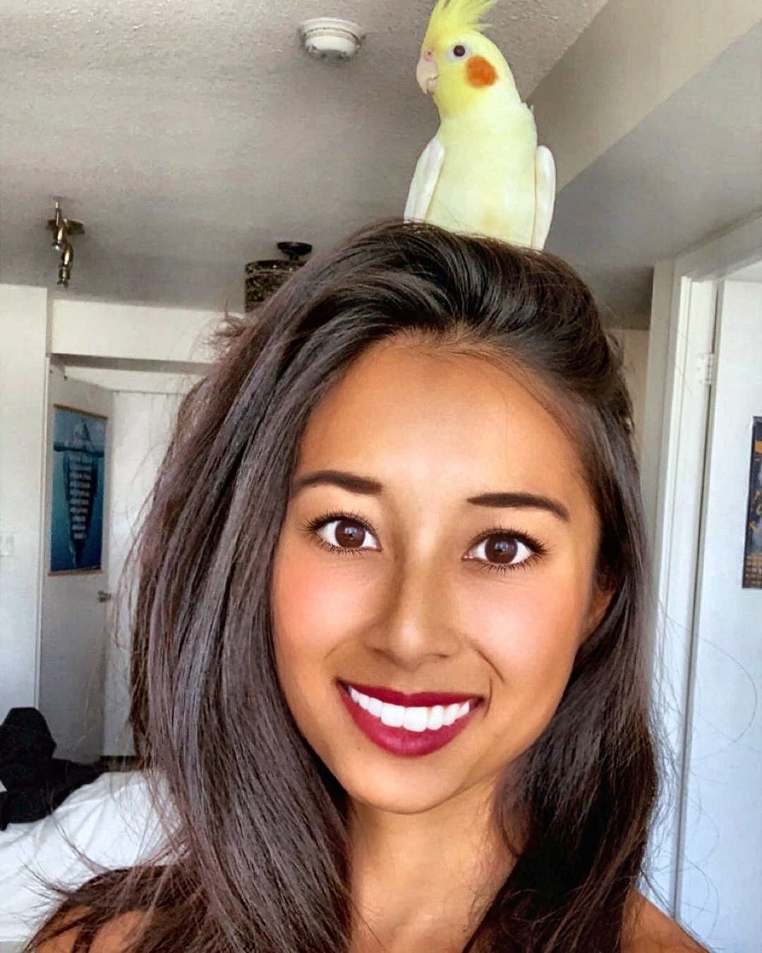 Samantha smiling with a cockatiel perched on her head
